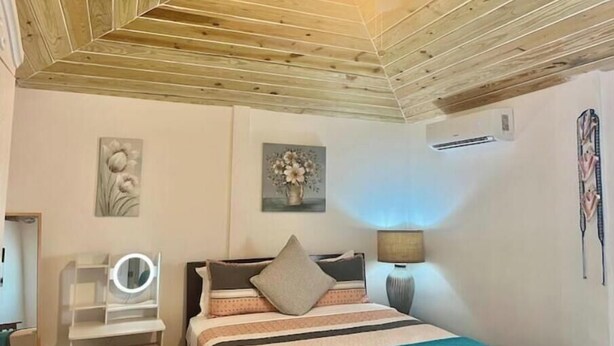 Un dormitorio con techo de madera, una cama con ropa de cama a rayas, un tocador con espejo y aire acondicionado de pared.