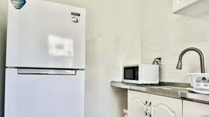 Una cocina con un refrigerador blanco, un microondas blanco y gabinetes blancos.