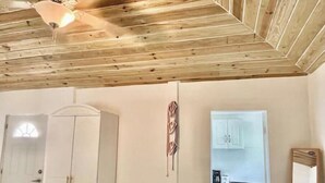 Una habitación con techo de madera, un armario, un espejo y una cocina visible a través de una puerta abierta.