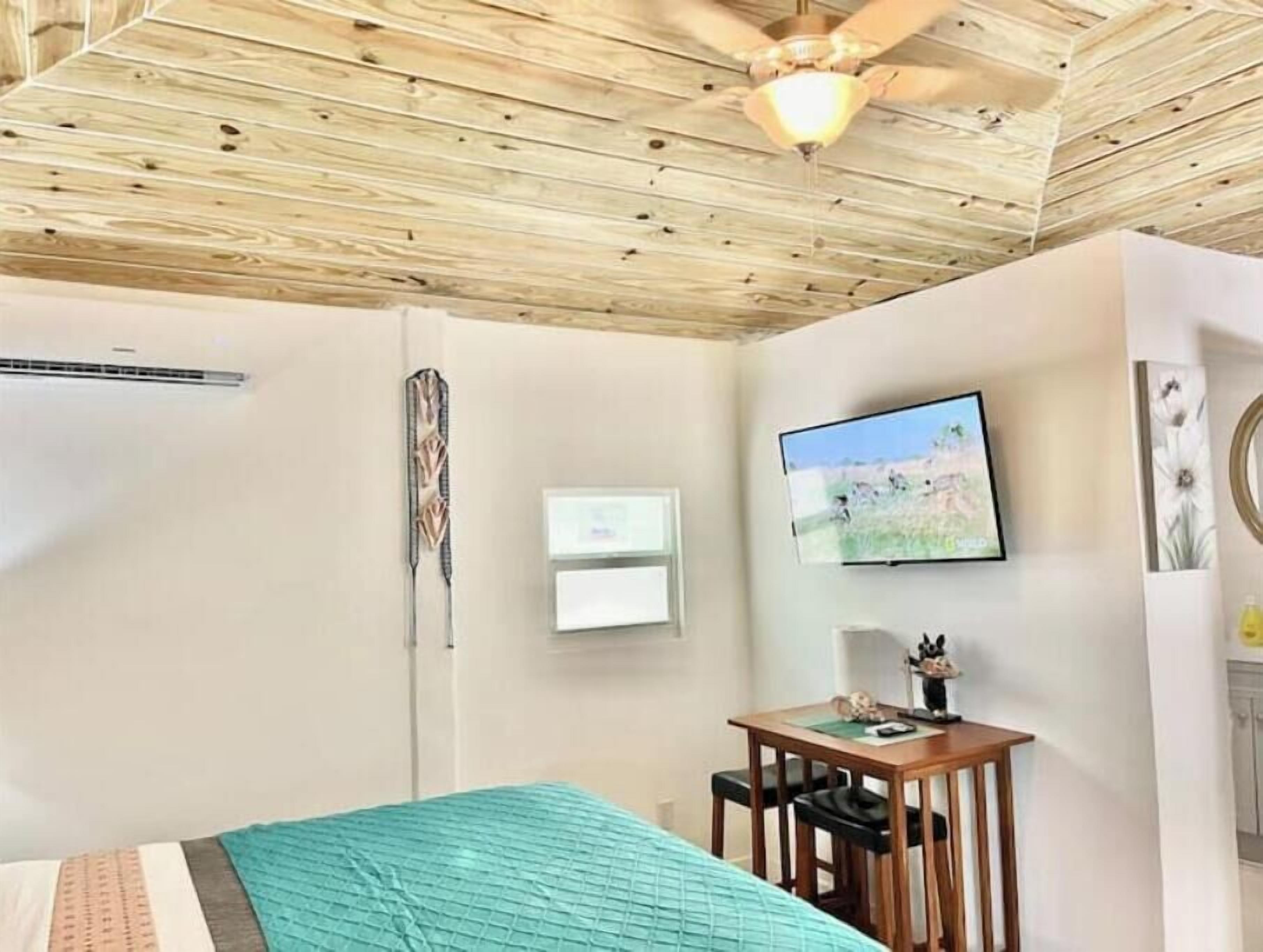 A bedroom with a bed, a ceiling fan, a TV, and a small table with chairs.