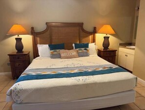 Een net opgemaakt bed met een kussen waarop 'WELCOME' staat, twee bedlampjes en een houten hoofdbord.