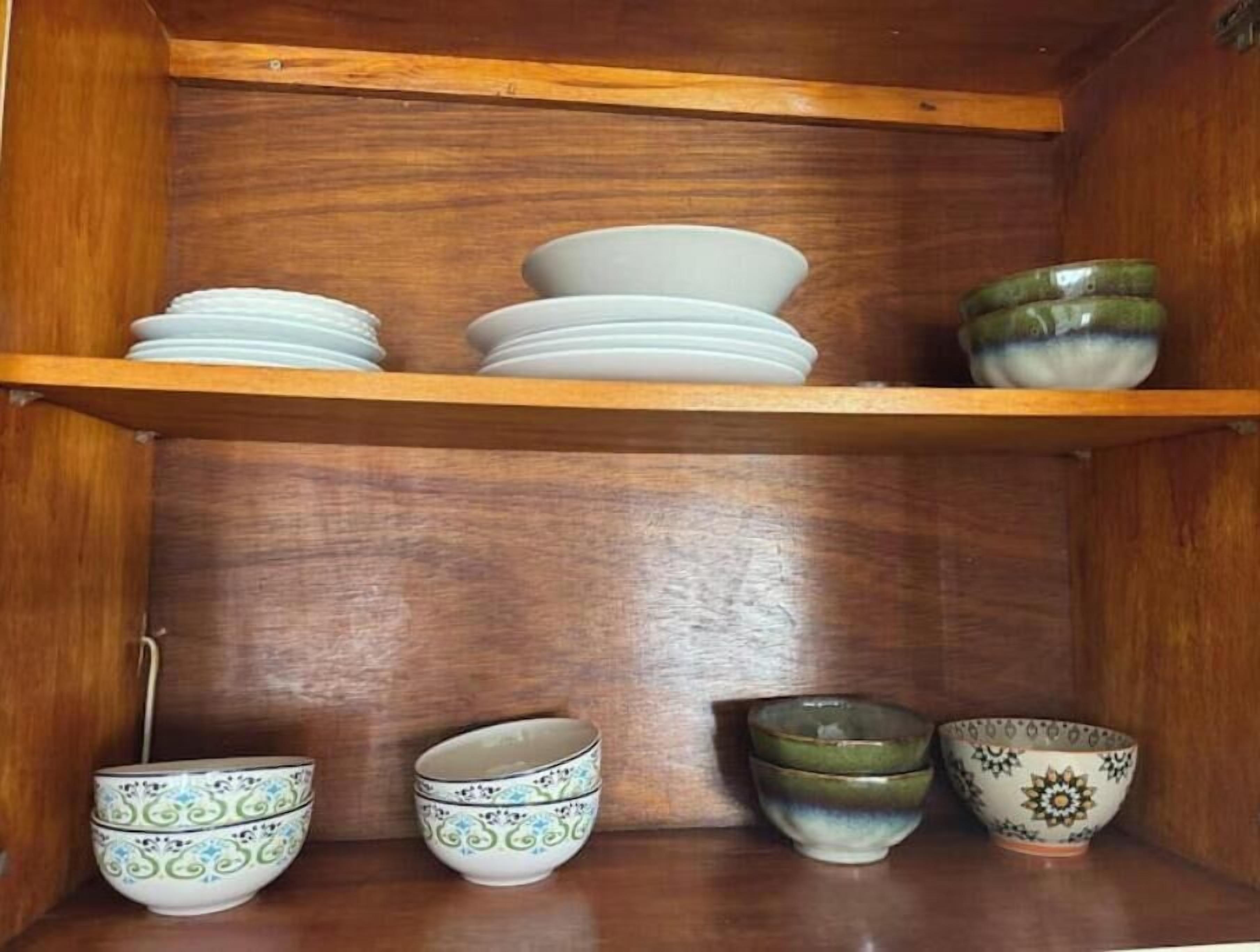 Une étagère en bois avec des bols et des assiettes blancs et verts.