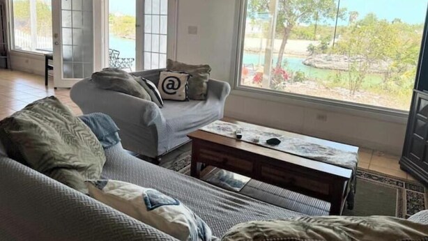 A living room with a sofa, a coffee table, and a view of a garden through large windows. - Waterfront 2-BR Home in Providenciales (Turtle Cove)