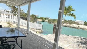 A covered outdoor area with a table and chairs, overlooking a body of water and a white fence. - Waterfront 2-BR Home in Providenciales (Turtle Cove)