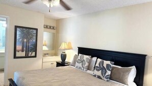 A bedroom with a bed, a ceiling fan, a nightstand with a lamp, a dresser, a mirror, and a framed picture on the wall. - Waterfront 2-BR Home in Providenciales (Turtle Cove)