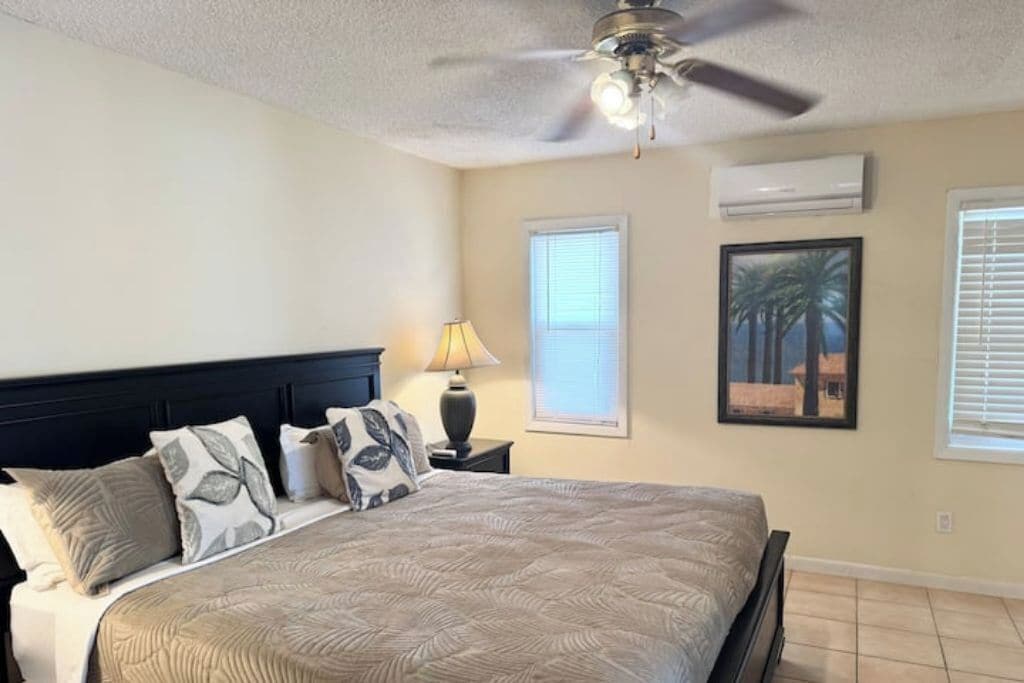 Une chambre à coucher comprenant un lit, un ventilateur de plafond, une fenêtre et un appareil de climatisation.