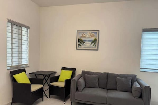 A living room with a grey sofa, two armchairs with yellow cushions, a small table, and a painting on the wall.
