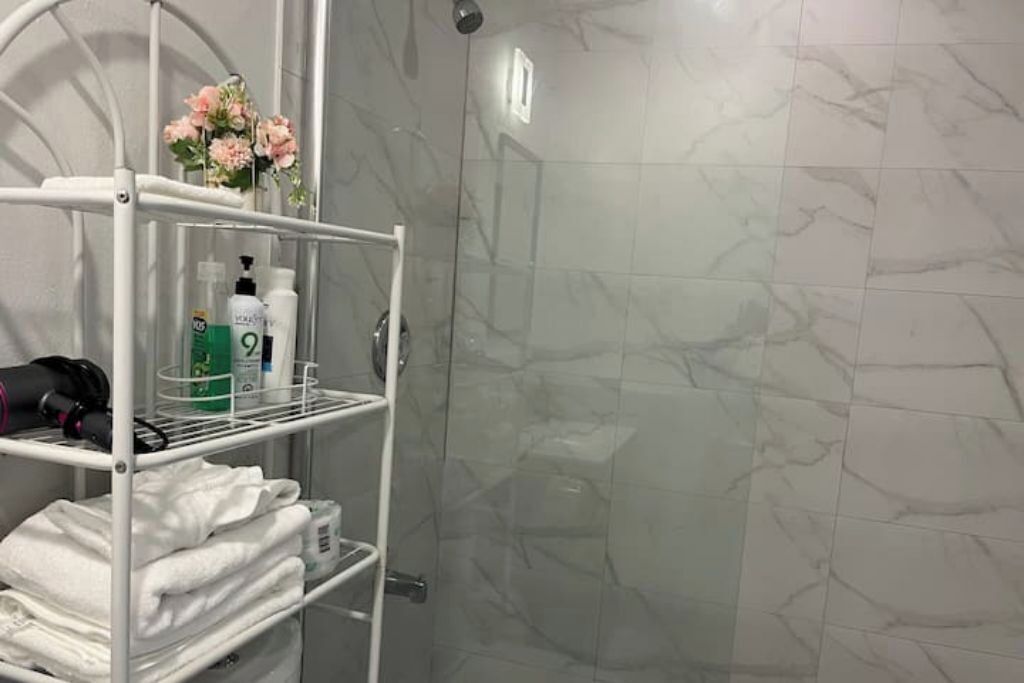 A bathroom with marble tiles, a white metal shelf with toiletries, and a vase with flowers.