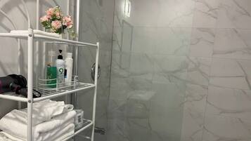 A bathroom with marble tiles, a white metal shelf with toiletries, and a vase with flowers.
