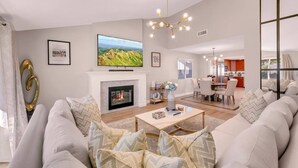 A modern living room with a fireplace, a television, and a dining area in the background.