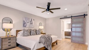 A modern bedroom with a bed, bedside tables, a ceiling fan, and a sliding glass door.