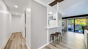 A spacious living area with a wooden floor, white walls, and a large sliding glass door leading to an outdoor patio. - This light-filled alpine retreat blends rustic charm with modern style. (Graeagle)