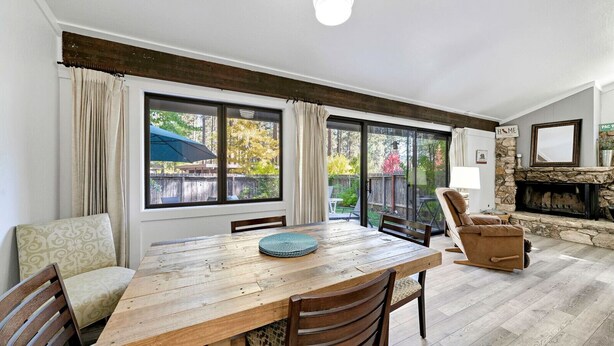 A dining area with a wooden table, chairs, and a sliding glass door leading to a patio. - This light-filled alpine retreat blends rustic charm with modern style. (Graeagle)