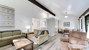 A spacious living room with a sofa, armchair, and a dining area with chairs and a table. - This light-filled alpine retreat blends rustic charm with modern style. (Graeagle)