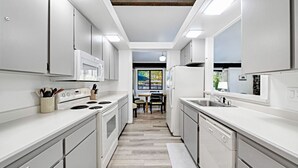 A modern kitchen with white cabinetry, a central island, and a dining area visible through the open door. - This light-filled alpine retreat blends rustic charm with modern style. (Graeagle)
