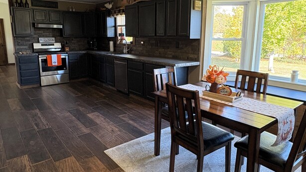 Una cocina moderna con armarios de madera oscura, electrodomésticos de acero inoxidable y un comedor con mesa y sillas de madera.