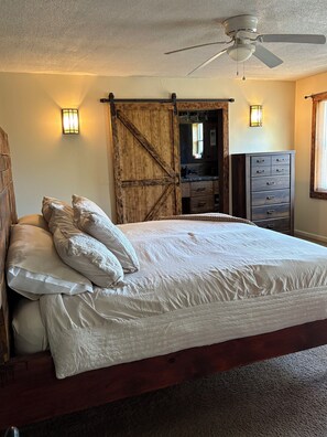 Une chambre à coucher avec un grand lit, une porte en bois de style grange, un ventilateur de plafond et une commode avec des tiroirs.