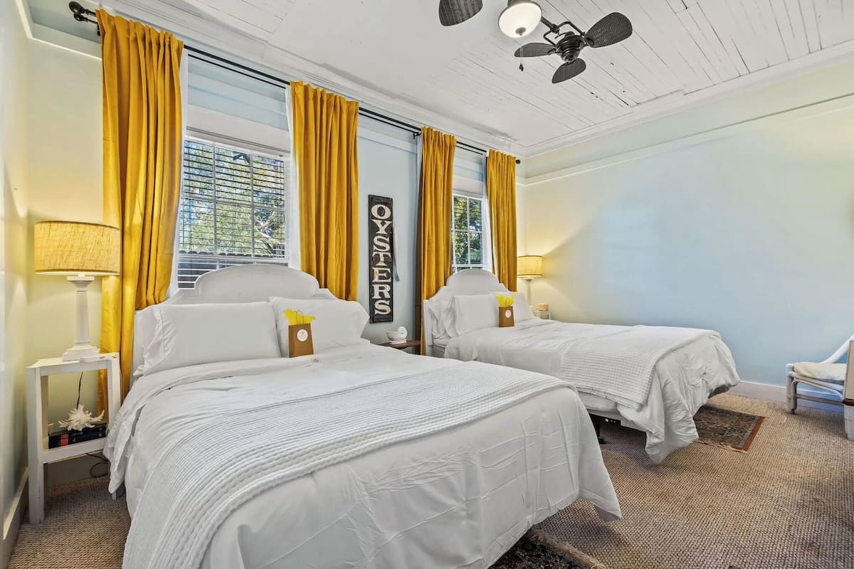A hotel room with two beds, yellow curtains, a ceiling fan, and a sign that says "OYSTERS".