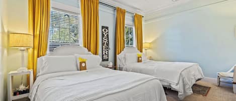 Habitación de hotel con dos camas, cortinas amarillas, ventilador de techo y un cartel que dice "OYSTERS".