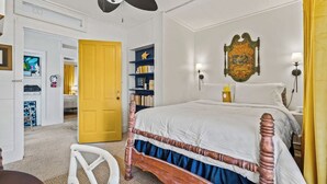 A bedroom with a wooden four-poster bed, a ceiling fan, a bookshelf, and a wall-mounted lamp. - The Old Carrabelle Hotel (Carrabelle)