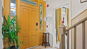 A yellow door with a window, a potted plant, a white wall-mounted light fixture, and a staircase with yellow curtains. - The Old Carrabelle Hotel (Carrabelle)