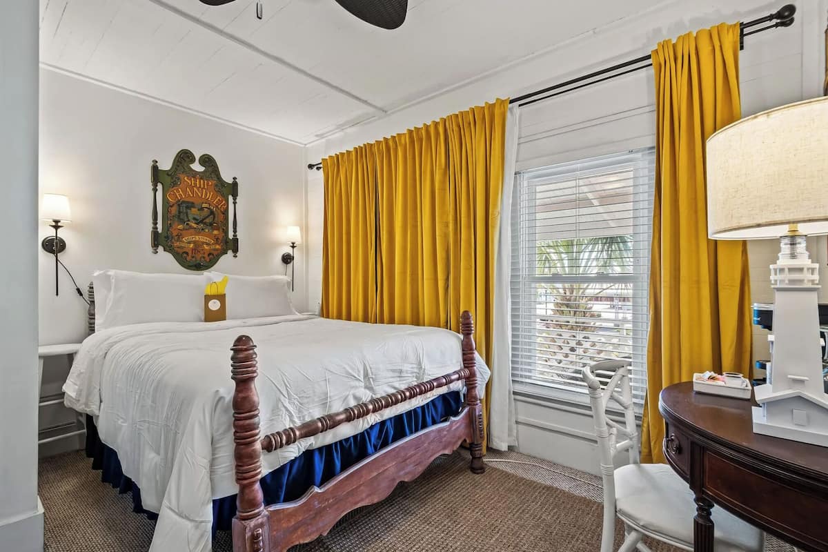 A bedroom with a wooden four-poster bed, yellow curtains, a wall-mounted ship-themed sign, and a window with blinds.