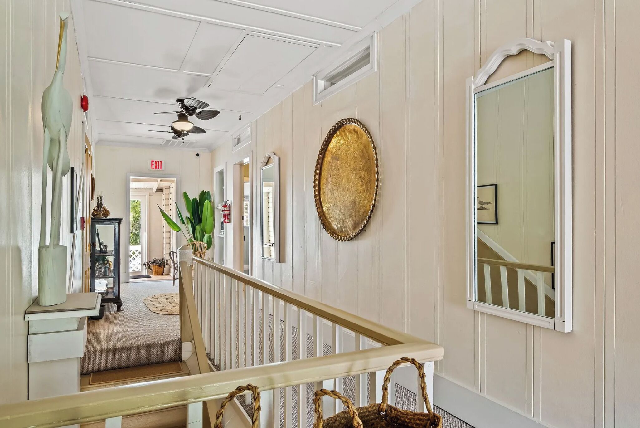 A hallway with a staircase, a ceiling fan, a large mirror, and a decorative plate on the wall.
