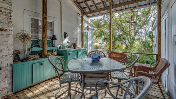 A covered patio with a table and chairs, a wooden ceiling fan, and a view of the surrounding greenery. - The Old Carrabelle Hotel (Carrabelle)