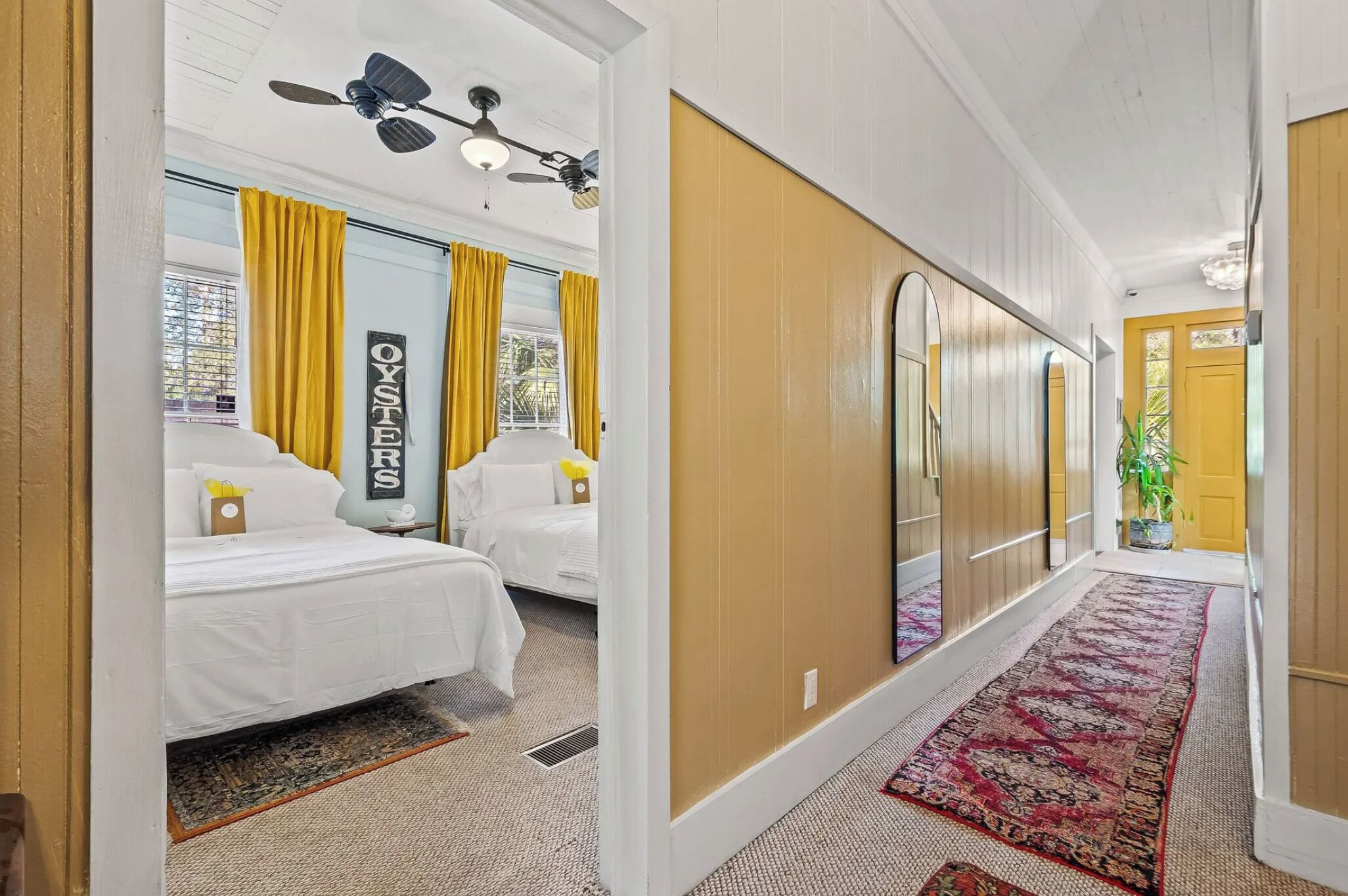 Ein Hotelzimmer mit zwei Betten, einem Deckenventilator, einem großen Spiegel und einer gelben Tür.