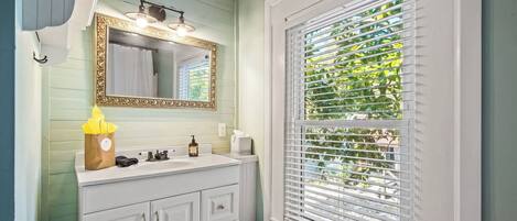 A bathroom with a white vanity, a gold-framed mirror, and a window with blinds.