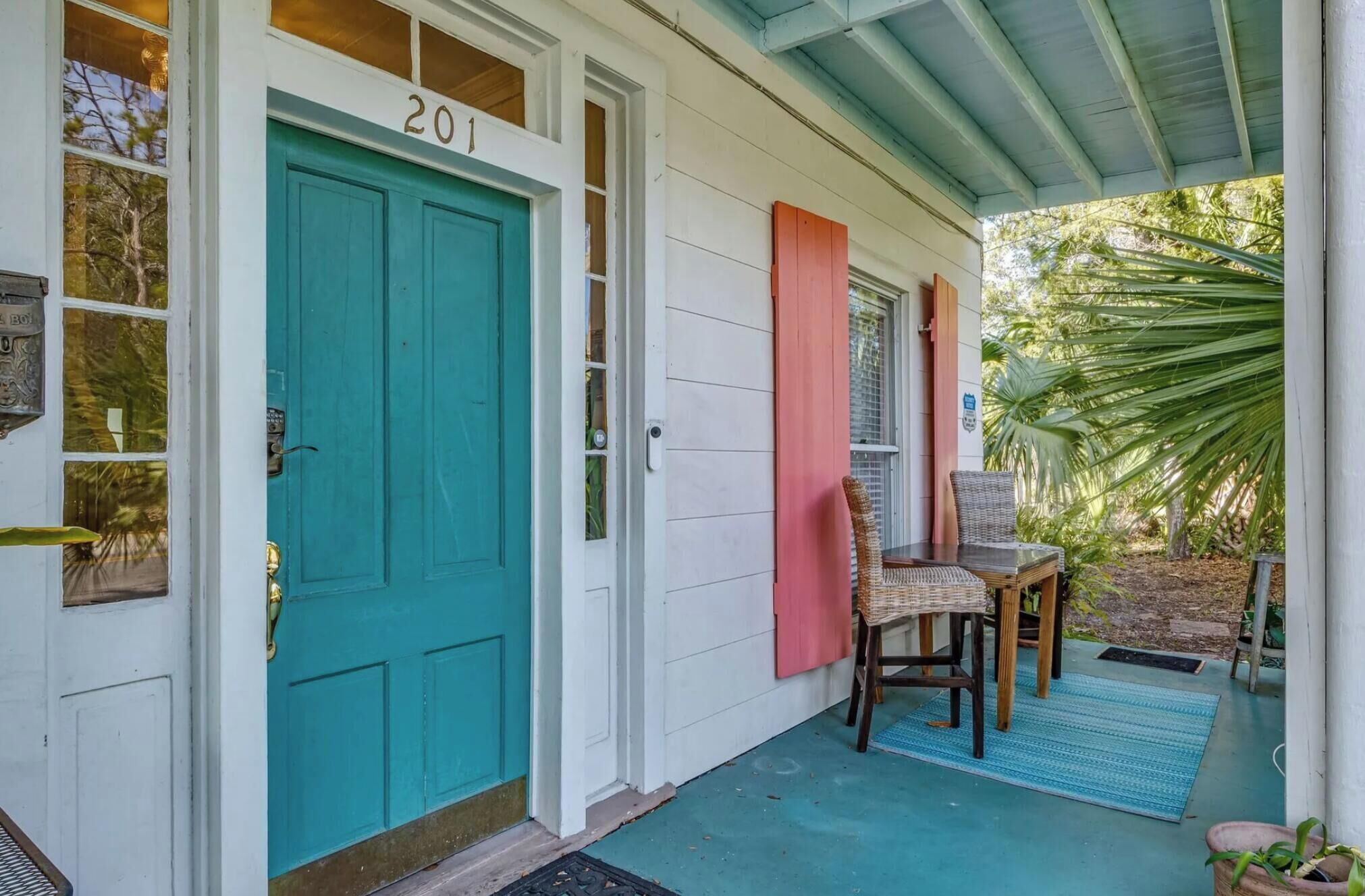 A turquoise door with the number 201, a covered porch with chairs, and a small table.