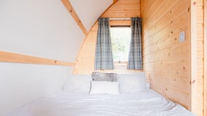 A bedroom with a wooden ceiling, a window with curtains, and a bed with white bedding. - Romantic Cosy Cabin with Hot Tub in Cumbria (Brampton)