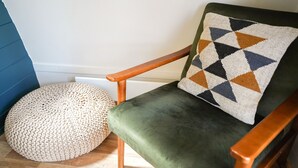 A green upholstered chair with a geometric-patterned pillow, a round woven ottoman, and a wooden armrest. - Romantic Cosy Cabin with Hot Tub in Cumbria (Brampton)