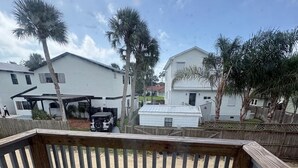Una terraza de madera con vista a una zona residencial, que incluye casas y una camioneta estacionada.