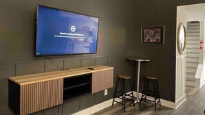 Una sala de estar moderna con un televisor de pantalla plana montado en la pared, un mueble de entretenimiento de madera debajo y dos taburetes de bar.
