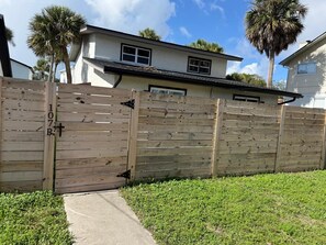 A residential property with a wooden fence, a concrete pathway, and a house with a white exterior and dark roof.