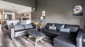 Una sala moderna con un sofá gris, una mesa de centro de mármol y un comedor con una cocina al fondo.