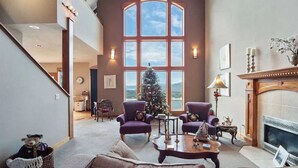 A spacious living room with a large window, a fireplace, and a Christmas tree. - 8,500 sq.ft. Luxurious River/Mountain View house (Kettle Falls)