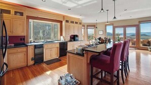 A spacious kitchen with wooden cabinets, a central island, and a large window offering a view of the outdoors. - 8,500 sq.ft. Luxurious River/Mountain View house (Kettle Falls)
