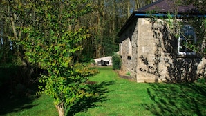 A stone building with a sloped roof, surrounded by a grassy yard and trees.