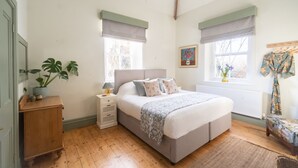 A bedroom with a bed, bedside tables, a nightstand, a potted plant, and a window with a view of trees.