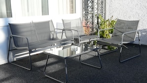 A patio with a glass table and four chairs, a small table with a glass, and a plant. - Gästehaus Tilly (Hann. Muenden)
