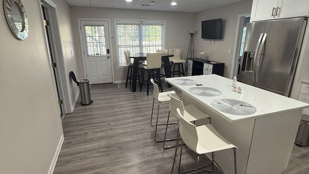 Una cocina moderna con una isla central, taburetes de bar, un refrigerador y un comedor con sillas y una mesa.