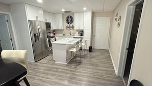 Una cocina moderna con armarios blancos, un refrigerador de acero inoxidable y una isla central con taburetes de bar.