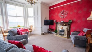 A living room with grey sofas, red cushions, a fireplace, and a TV. - Llety - sleeps 2 guests  in 1 bedroom (Criccieth)
