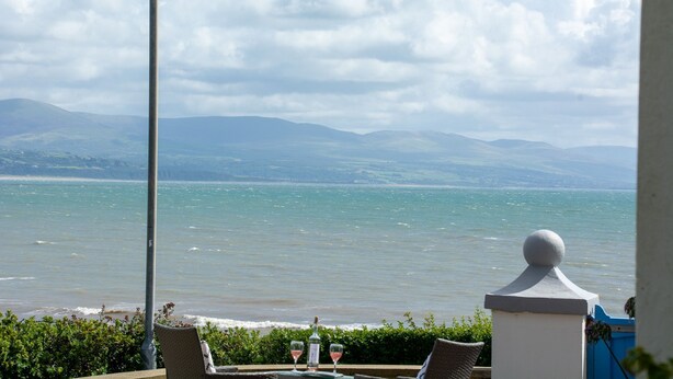 A seaside view from a balcony with a table set for two, overlooking the sea and distant hills. - Llety - sleeps 2 guests  in 1 bedroom (Criccieth)