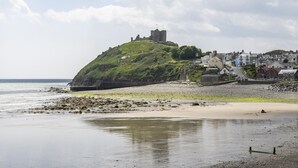 A coastal town with a historic castle on a hill, a sandy beach, and residential buildings. - Llety - sleeps 2 guests  in 1 bedroom (Criccieth)