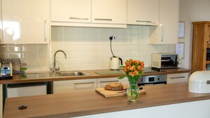 Une cuisine moderne avec des meubles blancs, un plan de travail en bois, un évier, une bouilloire, un grille-pain et un four à micro-ondes.