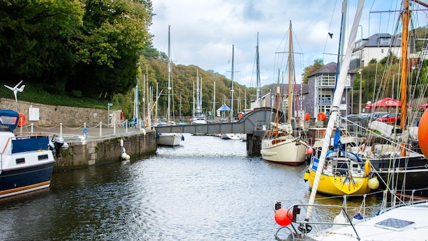 Un port de plaisance où des bateaux sont amarrés le long d’un canal étroit, entouré d’arbres et de bâtiments.