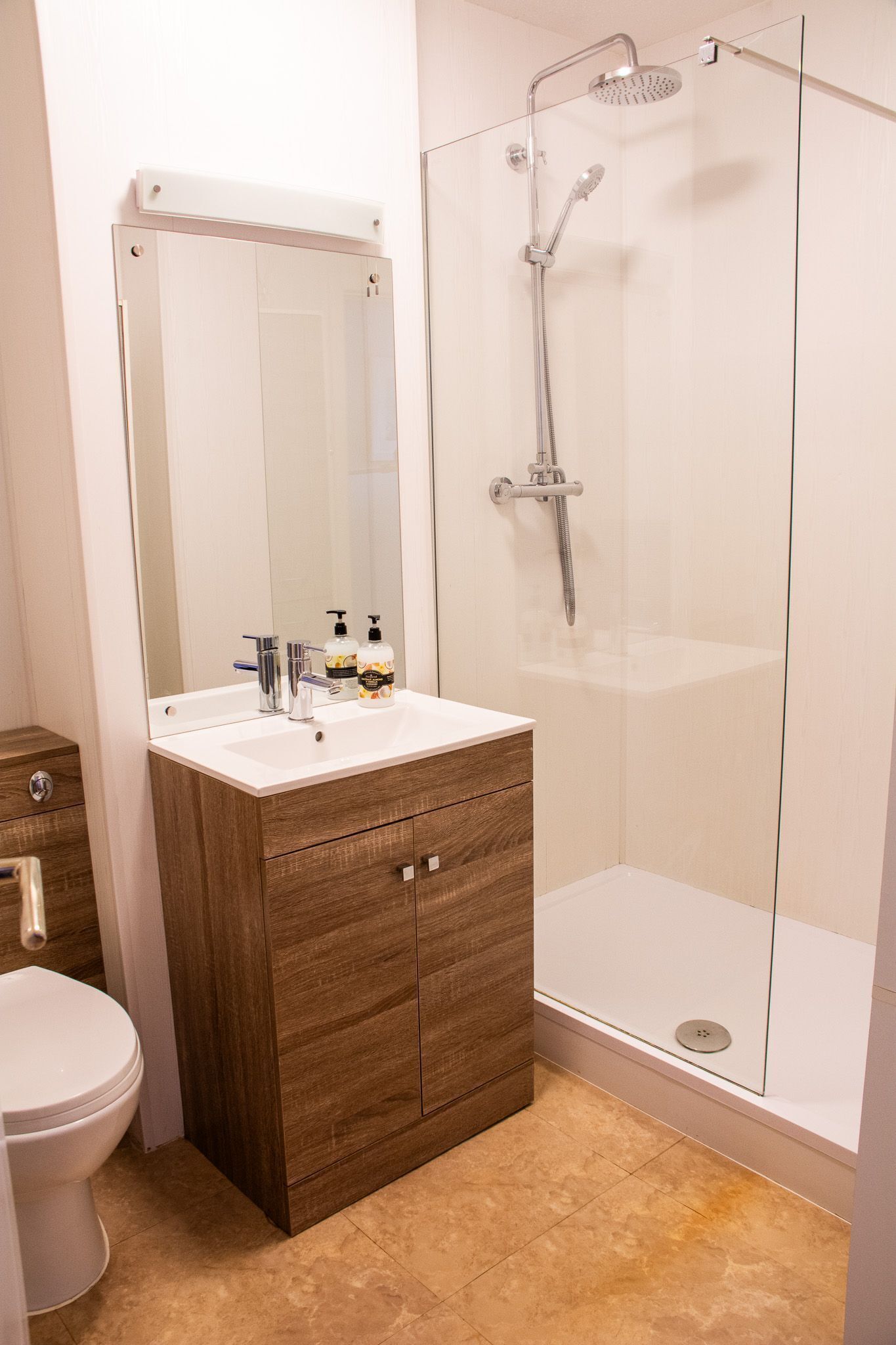 A bathroom with a wooden vanity, a white sink, a mirror, a shower enclosure, and a toilet.